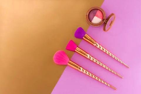 Three brushes and eyeshadow on a double purple - copper-gold background. Stock Photos
