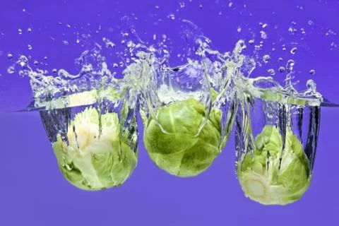 Three brussels sprouts falling in water with air bubbles Foto stock