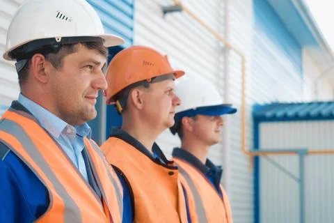 Three builders in helmets and vests stand in row. Friendly construction team of Stock Photos