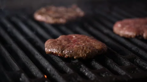 Three burgers are cooked on an open flame grill. Burgers are brown and sizzling. Vídeo Stock 284672876
