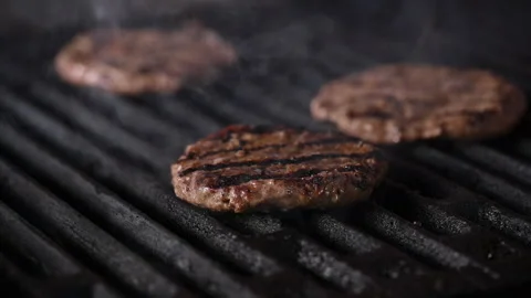 Three burgers are cooked on an open flame grill. Burgers are brown and sizzling. Vídeo Stock 284673046