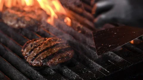 Three burgers are cooked on an open flame grill. Burgers are brown and sizzling. Stock Footage 284673535