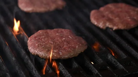 Three burgers are cooked on an open flame grill. Burgers are brown and sizzling. Stock Footage 284673742