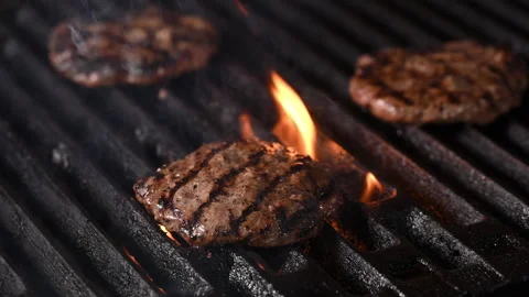 Three burgers are cooked on an open flame grill. burgers are brown and sizzling. 動画素材 284674286