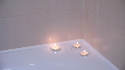 Three burning candles on the edge of bath in bathroom, close-up view. Stock Footage 272911292