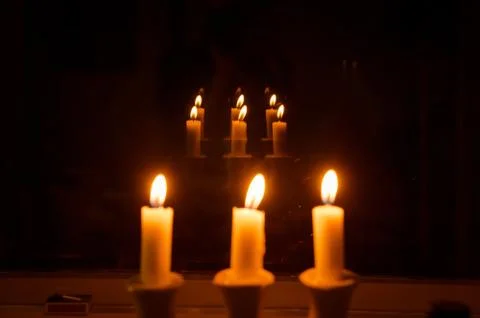Three burning candles in reflections. Flame of a candle on a dark background. Stock Photos