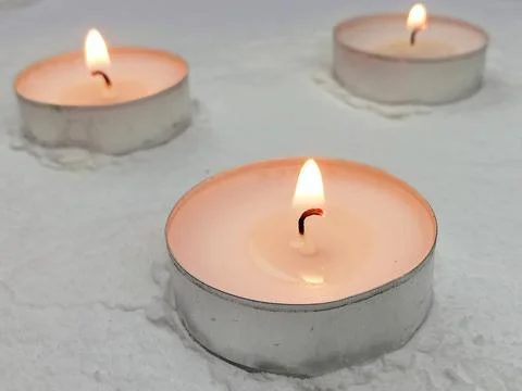 Three Burning Tea Light Candles on Snow Background Stock Photos