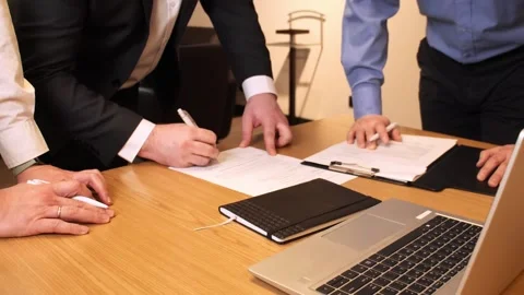 Three businessmen engage in process of signing papers while standing next to Vidéo 270164269