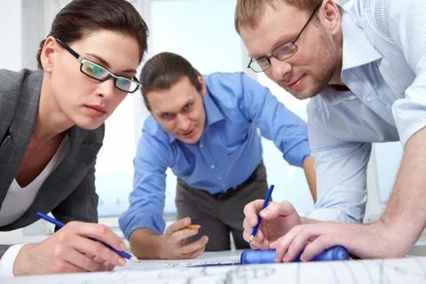 Three businesspeople with pencils bending over a draft Stock Photos