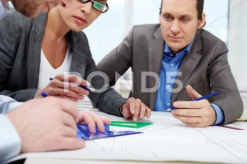 Three businesspeople sitting at table and sketching a project Stock Photos