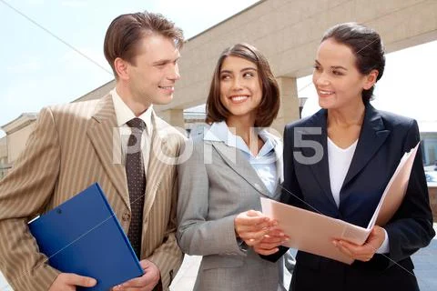 Three businesspeople standing outdoors with folders and talking Stock-Fotos