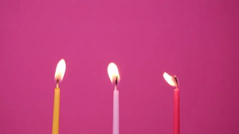 Three cake candles burning on a pink background. Close up on yellow, pink and Stock Footage 162503014