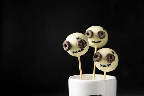Three cake pops balls with the faces of happy monsters on a black background Stock Photos