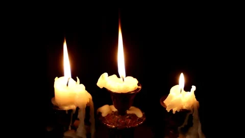 Three candles burn in a candlestick on a black background. Wind blowing Stock Footage 115284323