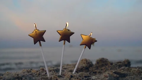 Three candles in form of star burn in sand on beach on background of blurred sea Stock Footage 167624143