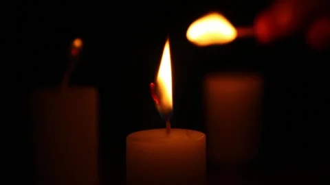 Three candles lit together with single match in dark scene Stock Footage 323340866