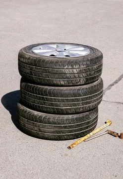 Three car wheels are on top of each other next to a tire wrench Stock Photos