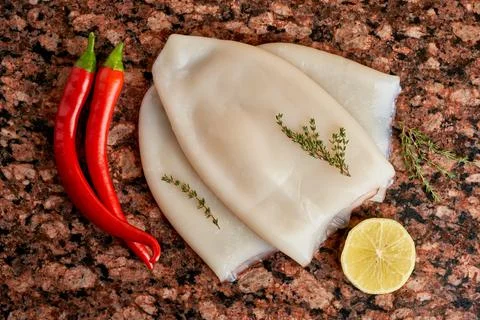 Three carcasses of fresh raw squid with lemon, pepper, thyme on a marble stone Stock Photos
