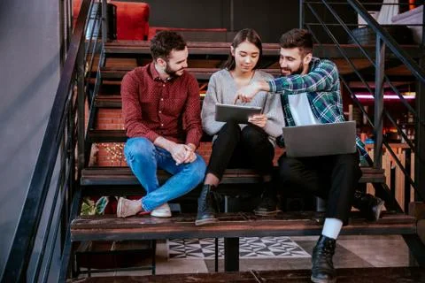Three charismatic young office workers working hard using tablet and notebook to Stock Photos