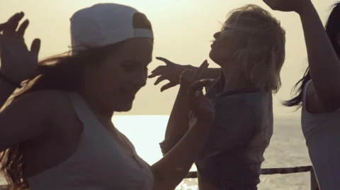 Three cheerful girls dressed in the same tights dancing at sunset near the sea Stock Footage 59973761