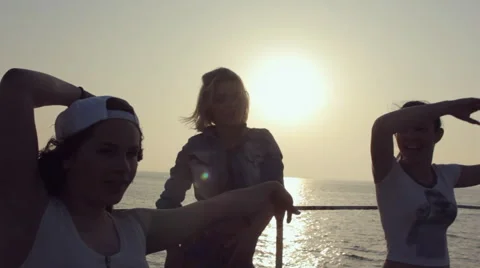 Three cheerful girls dressed in the same tights dancing at sunset near the sea Stock Footage 59973776