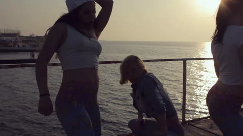 Three cheerful girls dressed in the same leggings dancing at sunset near the sea Stock Footage 59973818