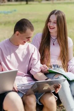 Three cheerful students study and work together outdoors on a sunny day, using 스톡 사진