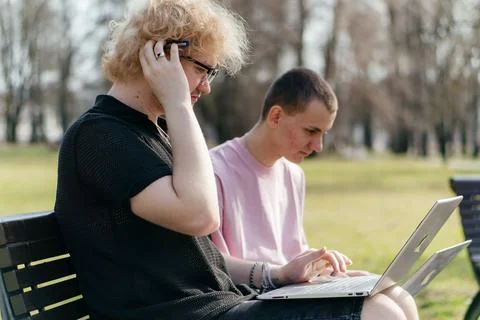 Three cheerful students study and work together outdoors on a sunny day, using Stock Photos