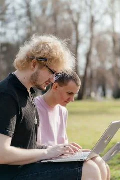 Three cheerful students study and work together outdoors on a sunny day, using Stock Photos
