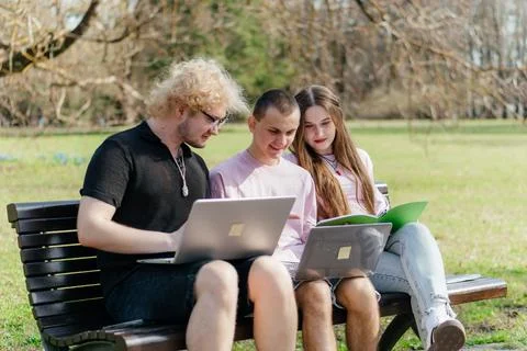 Three cheerful students study and work together outdoors on a sunny day, using Stock Photos