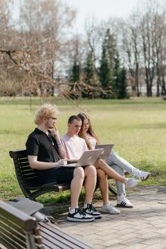 Three cheerful students study and work together outdoors on a sunny day, using Stock Photos