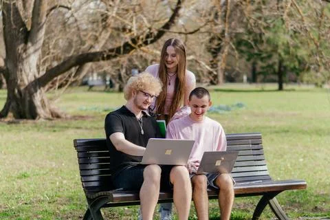 Three cheerful students study and work together outdoors on a sunny day, using Stock Photos