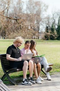 Three cheerful students study and work together outdoors on a sunny day, using Stock Photos