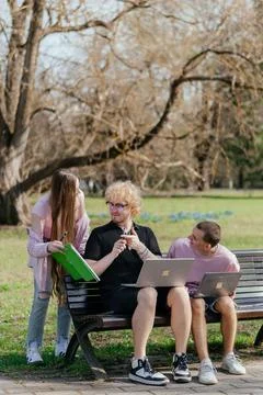 Three cheerful students study and work together outdoors on a sunny day, using Stock Photos