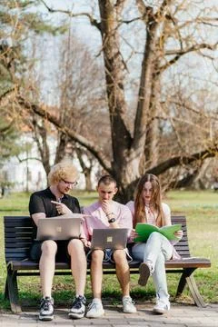 Three cheerful students study and work together outdoors on a sunny day, using Foto stock