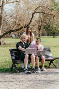 Three cheerful students study and work together outdoors on a sunny day, using Stock Photos