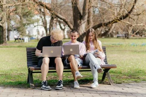Three cheerful students study and work together outdoors on a sunny day, using Foto stock