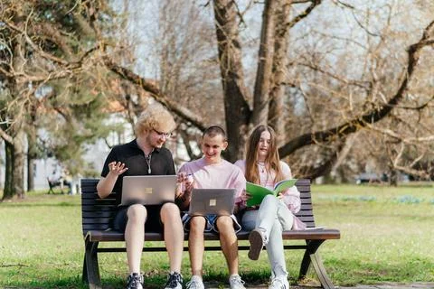 Three cheerful students study and work together outdoors on a sunny day, using Stock Photos