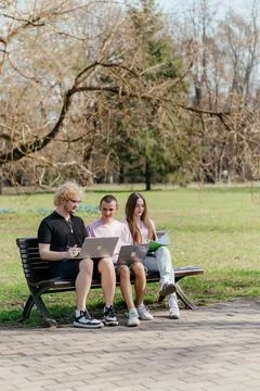 Three cheerful students study and work together outdoors on a sunny day, using Foto stock
