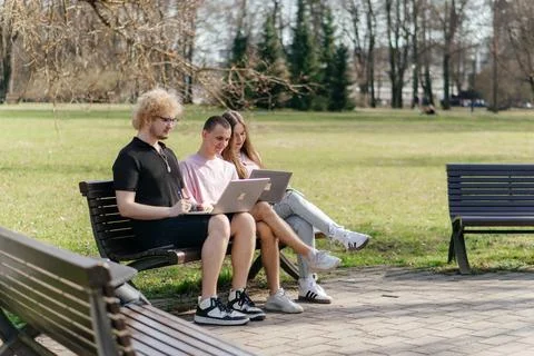 Three cheerful students study and work together outdoors on a sunny day, using Stock Photos