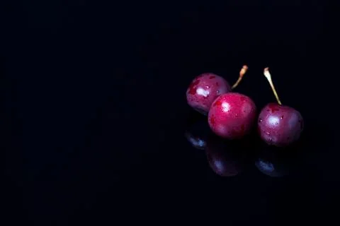 Three cherries on a black mirror background. Reflection, close-up, copy space 库存照片