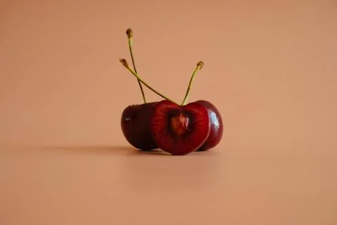 Three cherries with one cut open on peach background Stock Photos