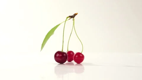 Three cherries with stems and green leaves rotate on a white background Stock Footage 135235092