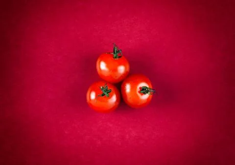 Three cherry tomatoes on red background. Stock Photos