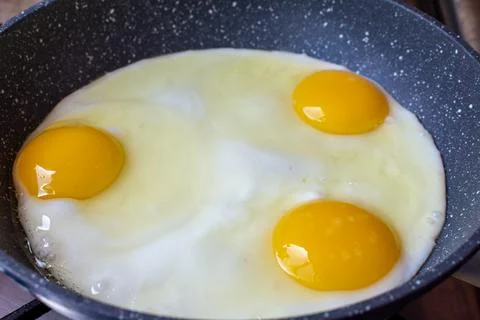 Three chicken eggs are fried in a frying pan Stock Photos