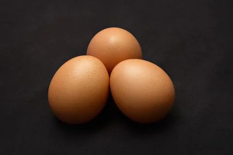 Three chicken eggs on a black background. Stock Photos