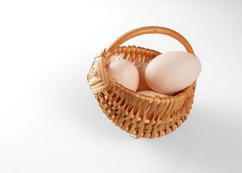 Three chicken eggs in a small wicker basket on a white background Stock Photos