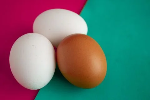 Three chicken eggs on table with green, turquoise and red background. Stock-Fotos