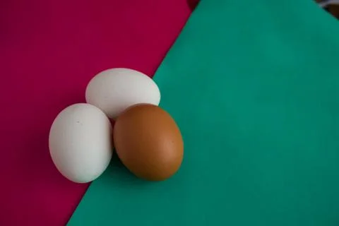 Three chicken eggs on table with green, turquoise and red background Stock-Fotos