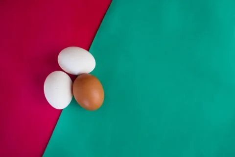 Three chicken eggs on table with green, turquoise and red background Stock-Fotos
